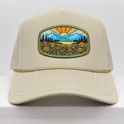 Port Sandz tan colored California Poppy Mesh-Back Trucker Hat. Vicose embroidered patch on front picturing sun and rays, mountains and California's State Flower, the golden poppy in fields. 